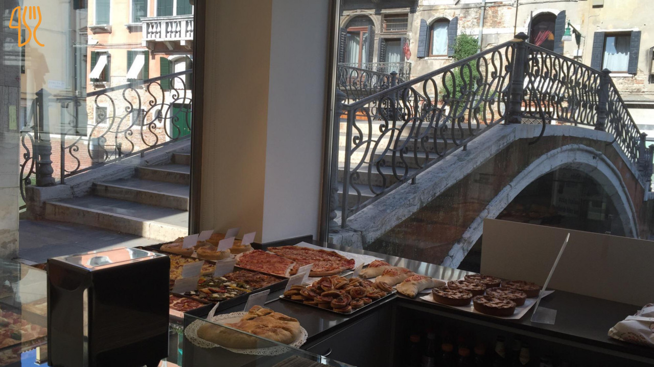 Banco interno con prodotti e finestra affacciata su un canale veneziano.